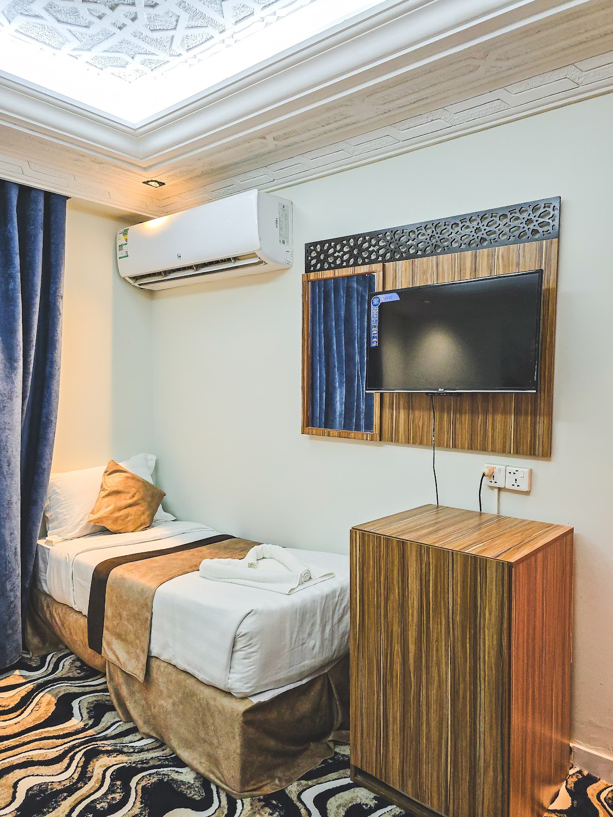 A clean and compact single room featuring a comfortable bed, air conditioning, and a wall-mounted television for a restful stay.