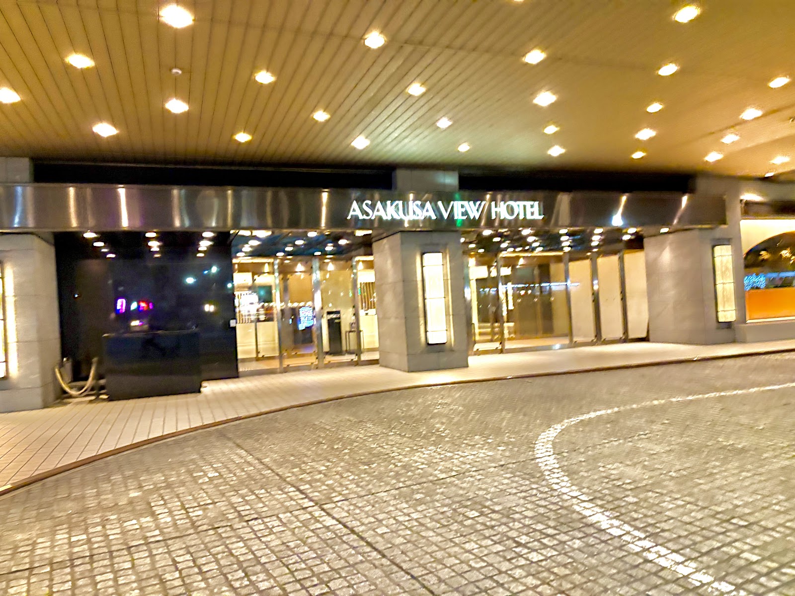A wide shot of the Asakusa View Hotel entrance area at night, highlighting the illuminated signage and curved drive-in path.