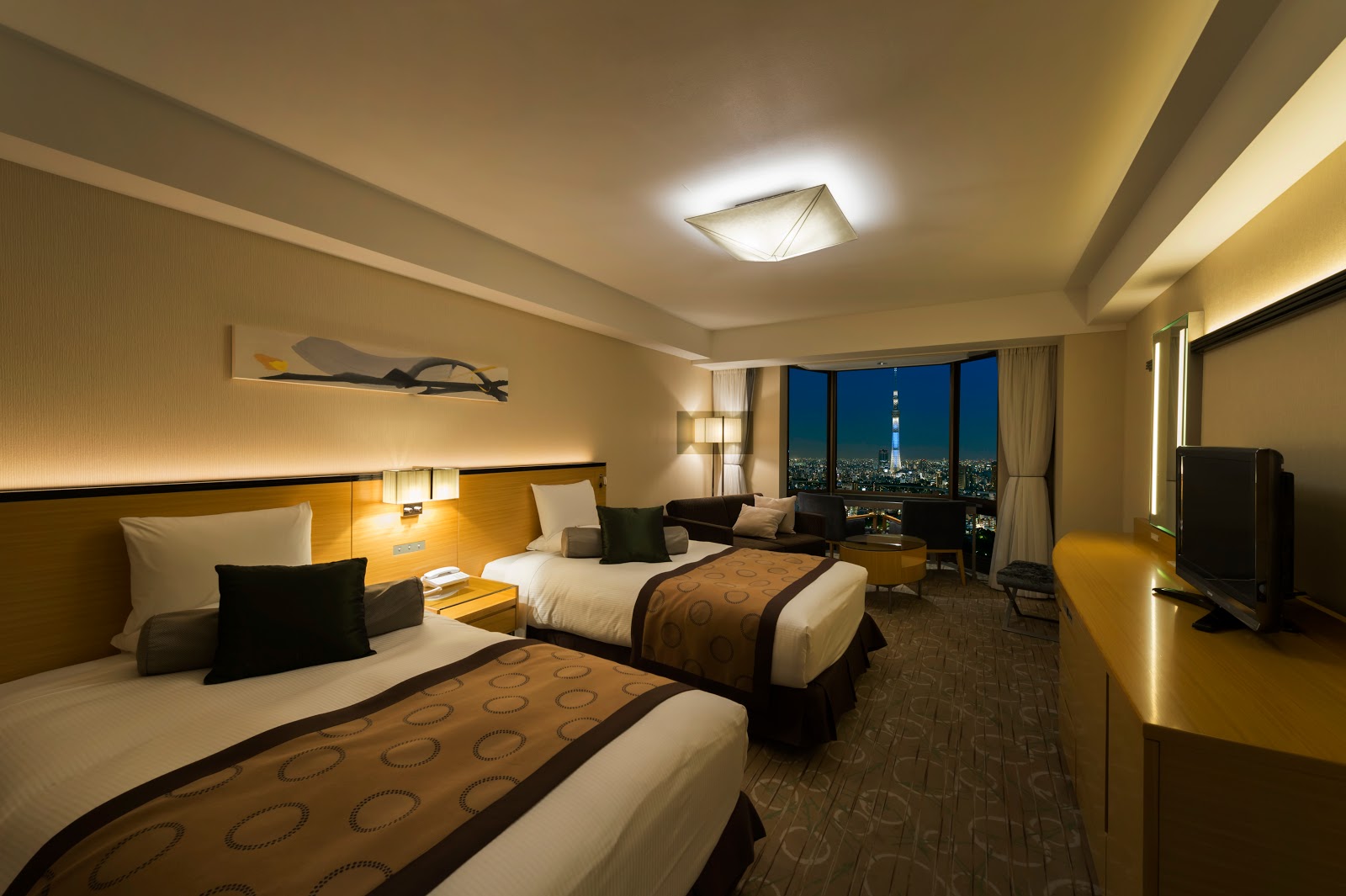 A comfortable twin guest room at Asakusa View Hotel, featuring two single beds, a cozy seating area, and a captivating nighttime city view of Tokyo Skytree.