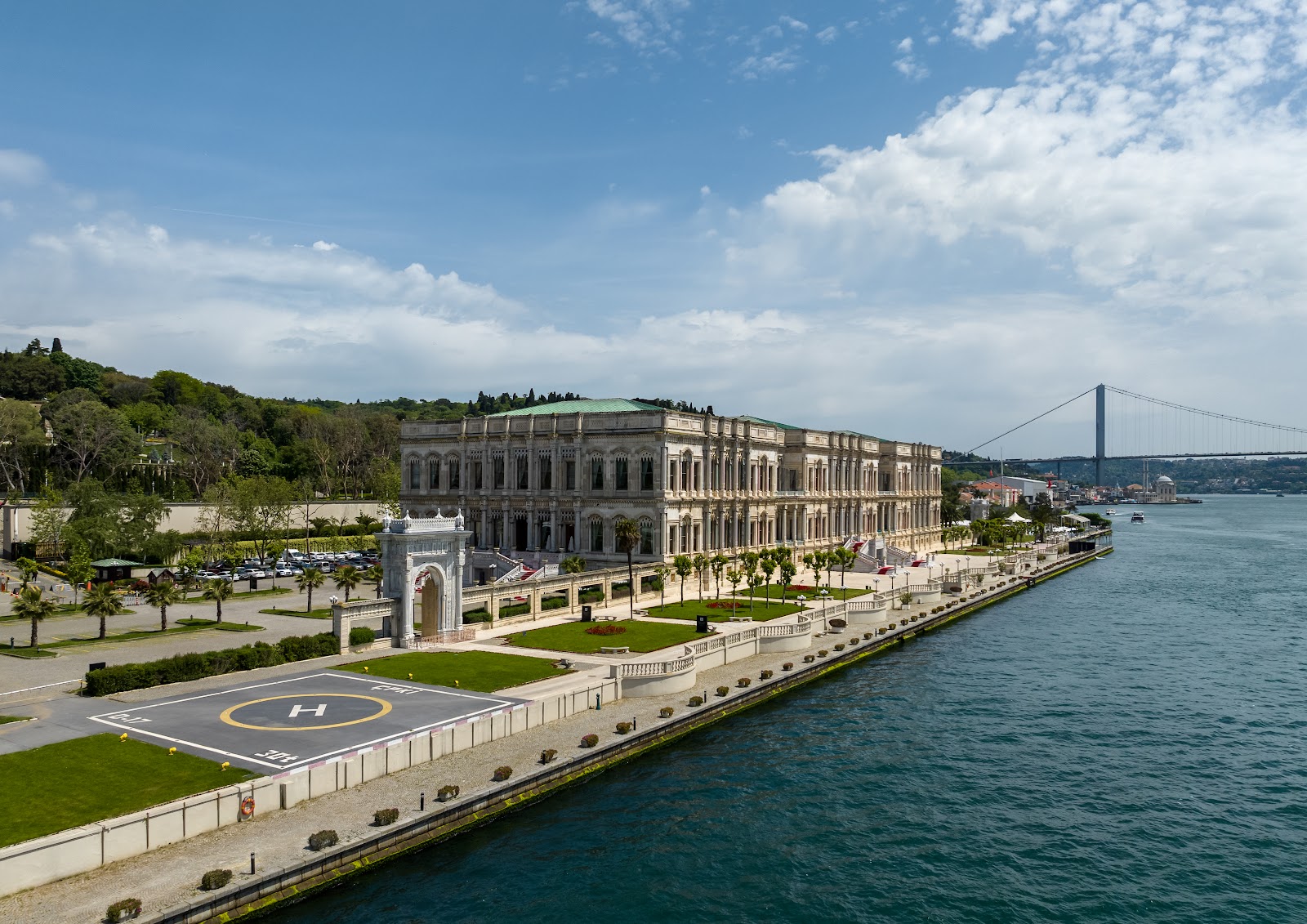 An expansive view of Ciragan Palace Kempinski, showcasing its extensive waterfront grounds, helipad, and the Bosphorus Bridge in the distance.