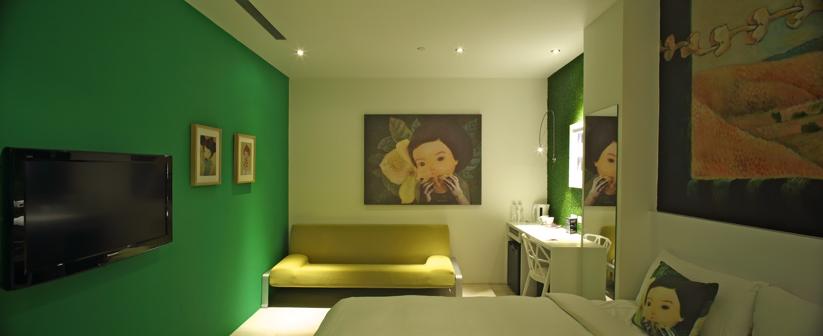 A contemporary guest room featuring a queen-size bed, a lime-green sofa, a desk area, and modern art pieces on a green accent wall.