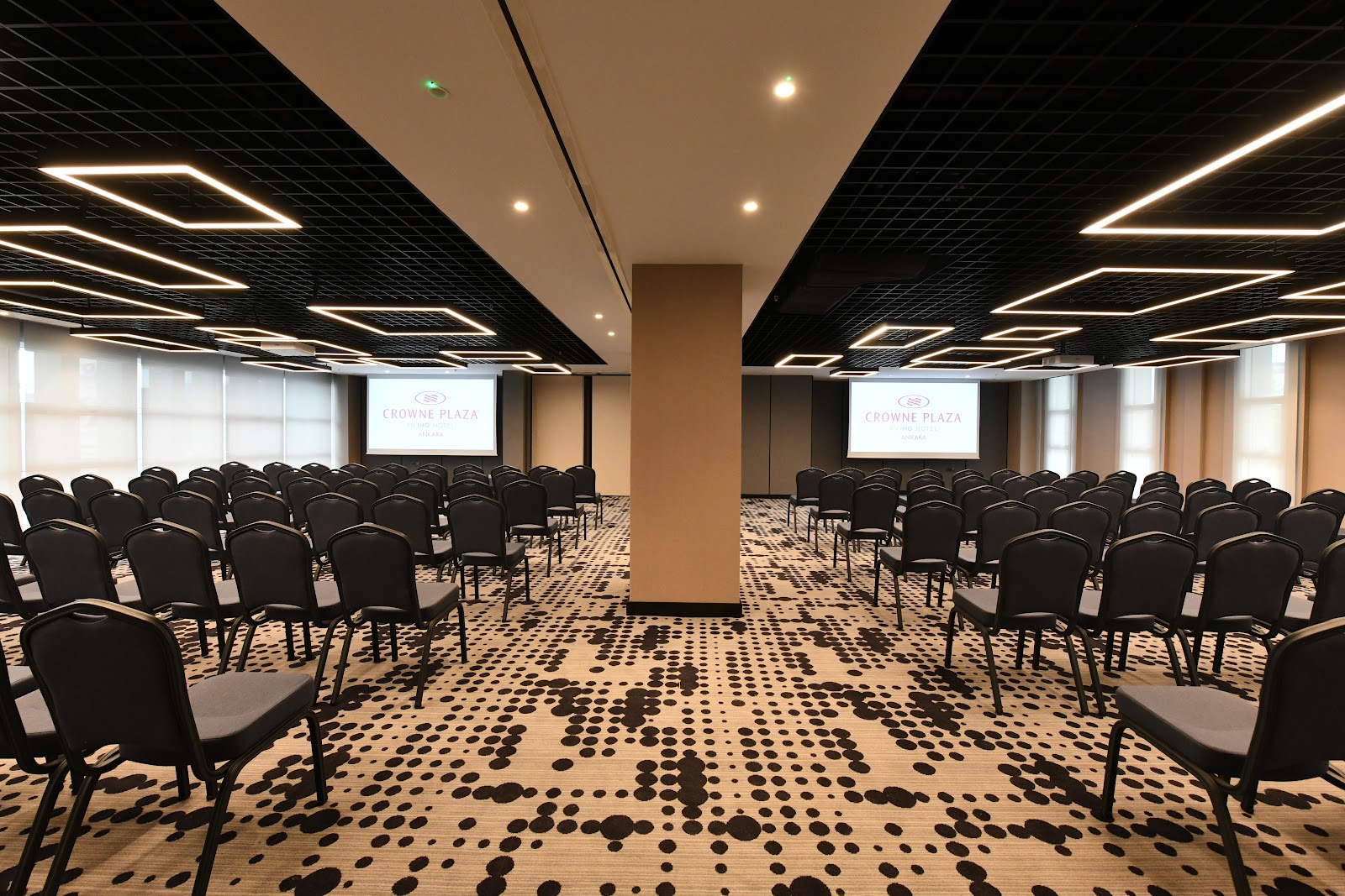 A modern meeting room or small conference hall with rows of chairs facing dual projection screens, featuring contemporary black ceiling design.