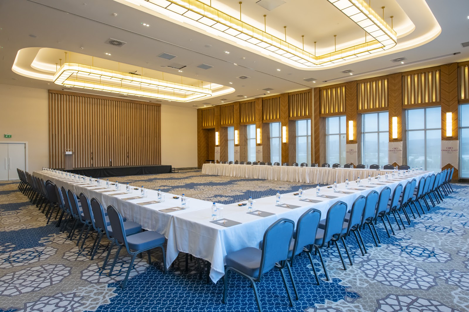 A large, bright conference or ballroom set up in a U-shape, featuring high ceilings, modern lighting, and large windows.