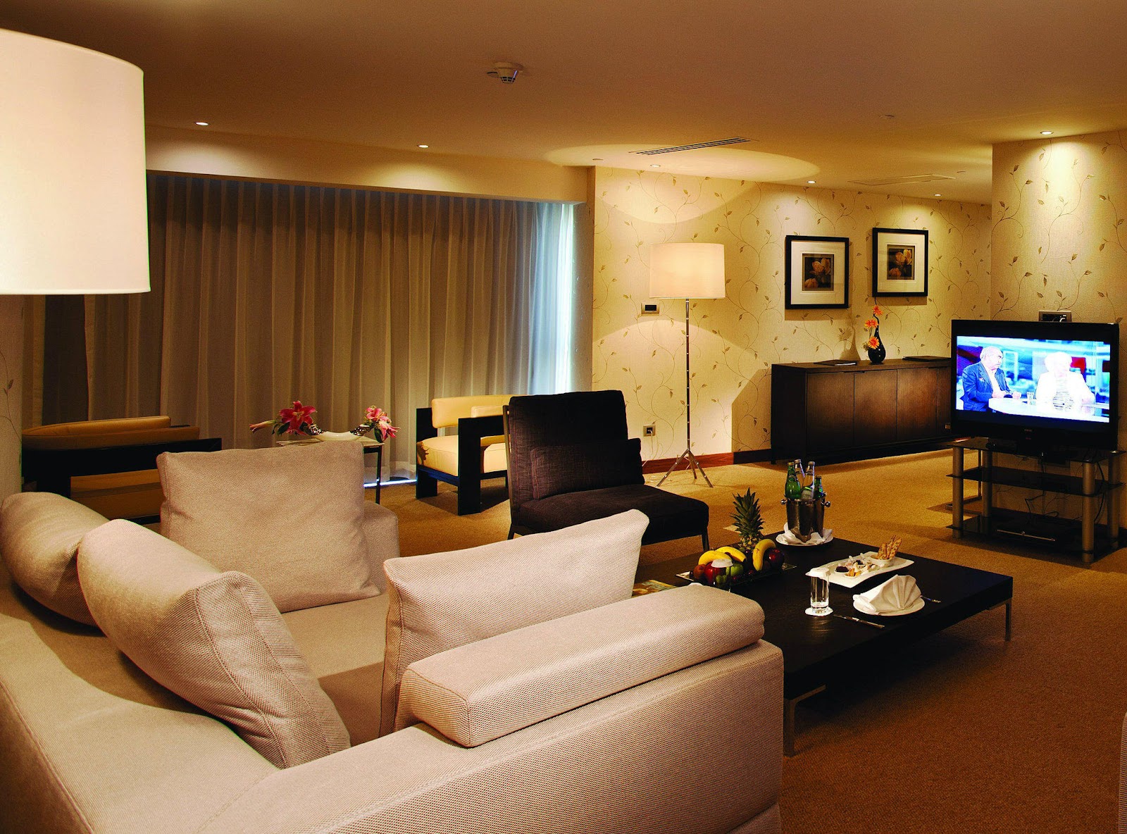 A spacious living area of a hotel suite with a large sofa, armchairs, and a TV.