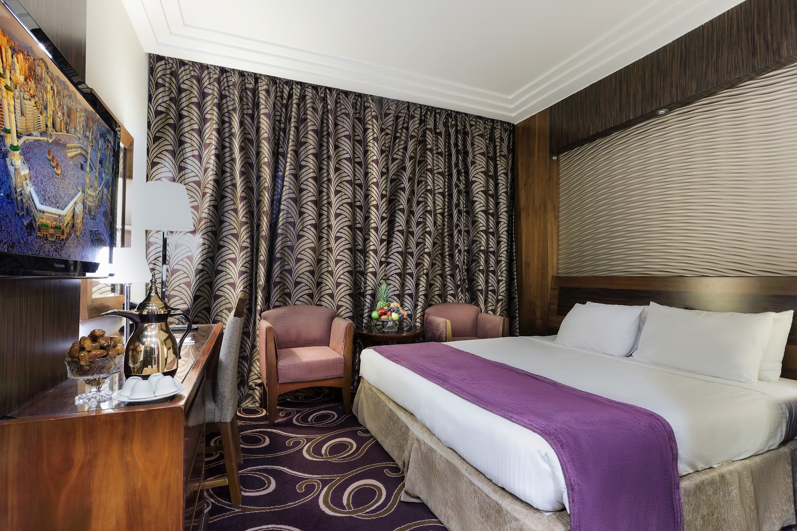A cozy king-size bedroom designed for comfort, featuring modern decor, a comfortable bed, and a TV displaying an image of the Kaaba, symbolizing the hotel's Makkah focus.