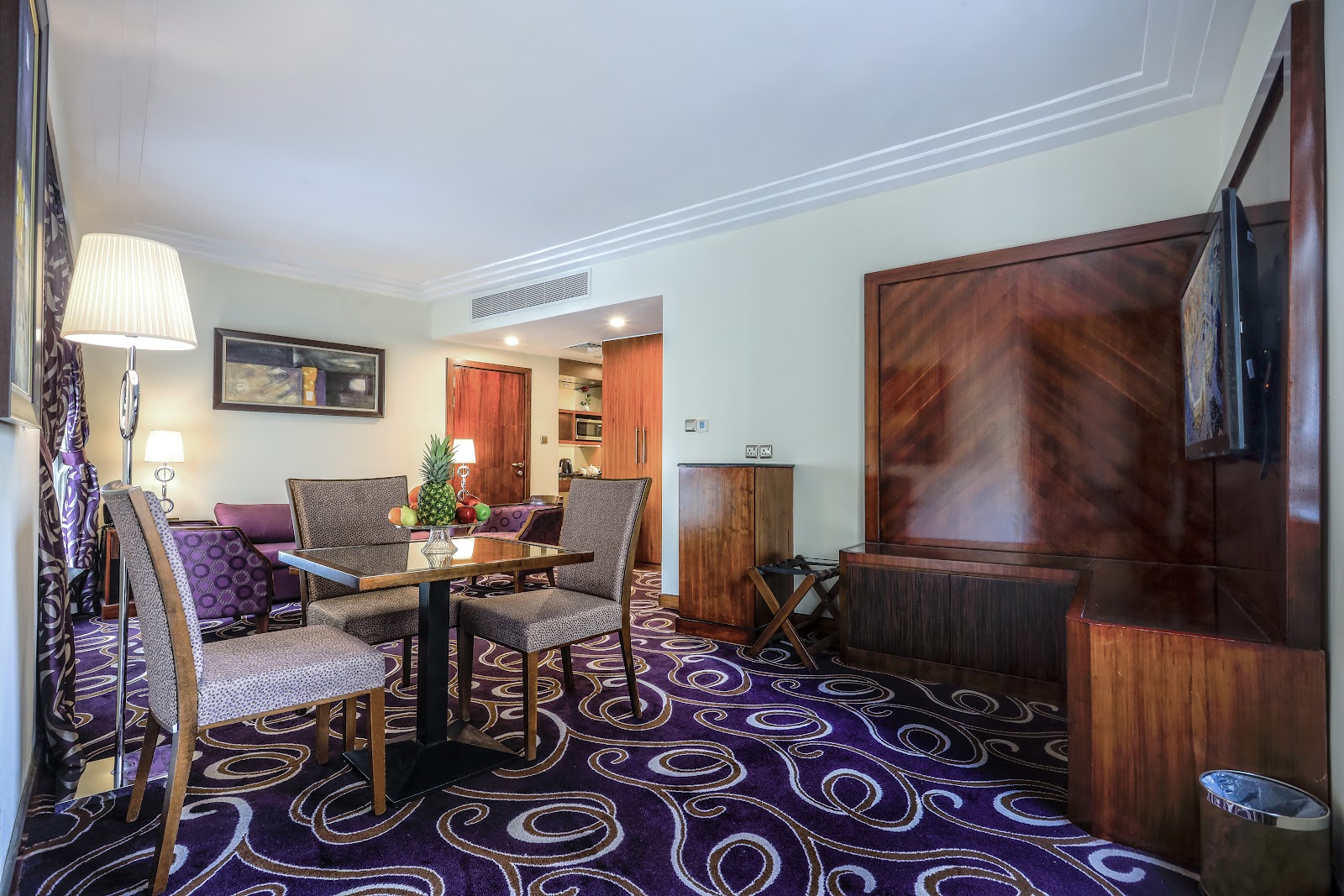 Another view of a spacious hotel suite living area, featuring a dining table, ample seating, and a flat-screen TV, designed for comfort and convenience.