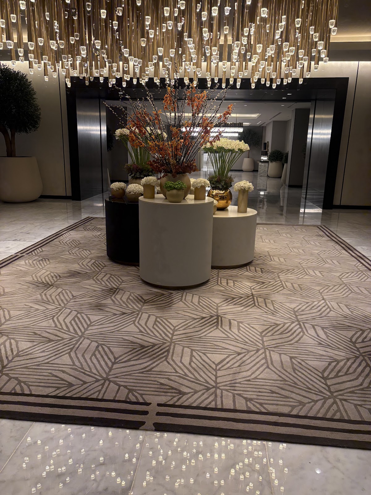 A sophisticated hotel lobby area with elegant decor, a large patterned rug, and a striking chandelier, indicating a high-end experience and a comfortable, welcoming space for pilgrims upon arrival.