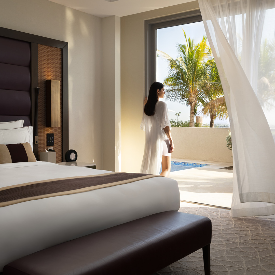 A luxury hotel room with a King-sized bed and direct access to a private outdoor plunge pool, viewed by a woman looking out.