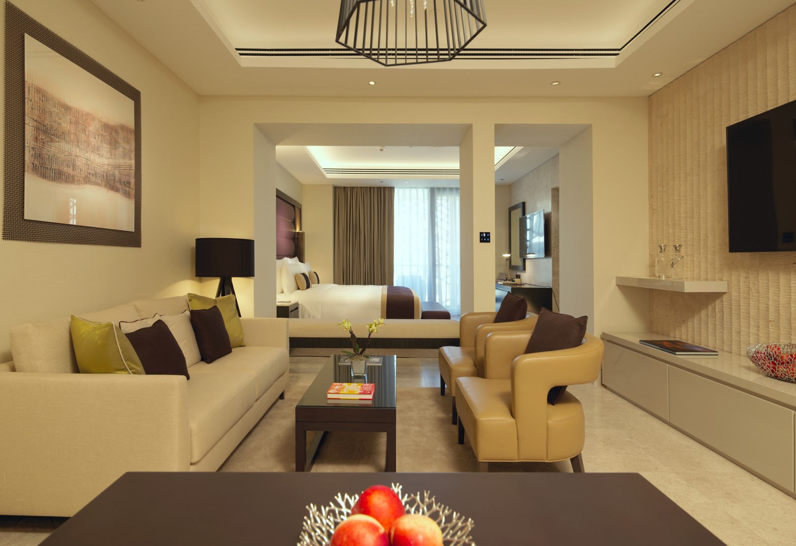 A spacious luxury suite featuring a separate living room area with a sofa and armchairs, connected to a bedroom.