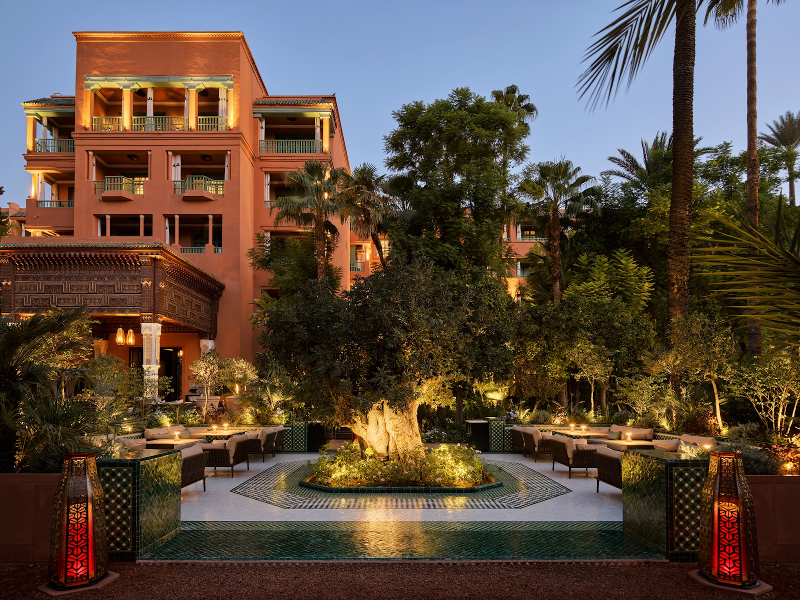 The hotel's palatial exterior seen from its extensive, beautifully lit gardens, with discreet outdoor dining areas visible.