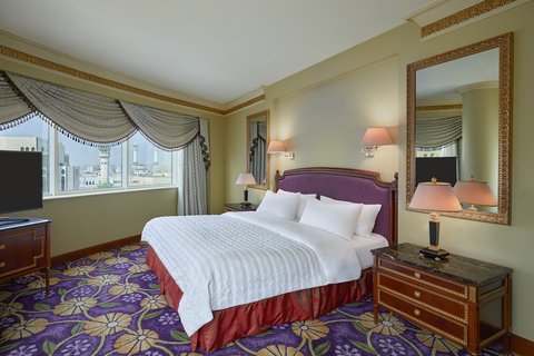 A comfortable King room featuring tasteful decor and a window offering a city view, including a distant minaret, indicating proximity to holy sites.