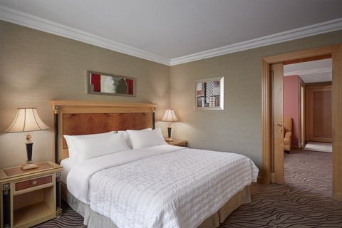 An elegant bedroom within a suite, featuring a comfortable king-size bed and sophisticated decor, with an adjoining door suggesting a larger multi-room accommodation.