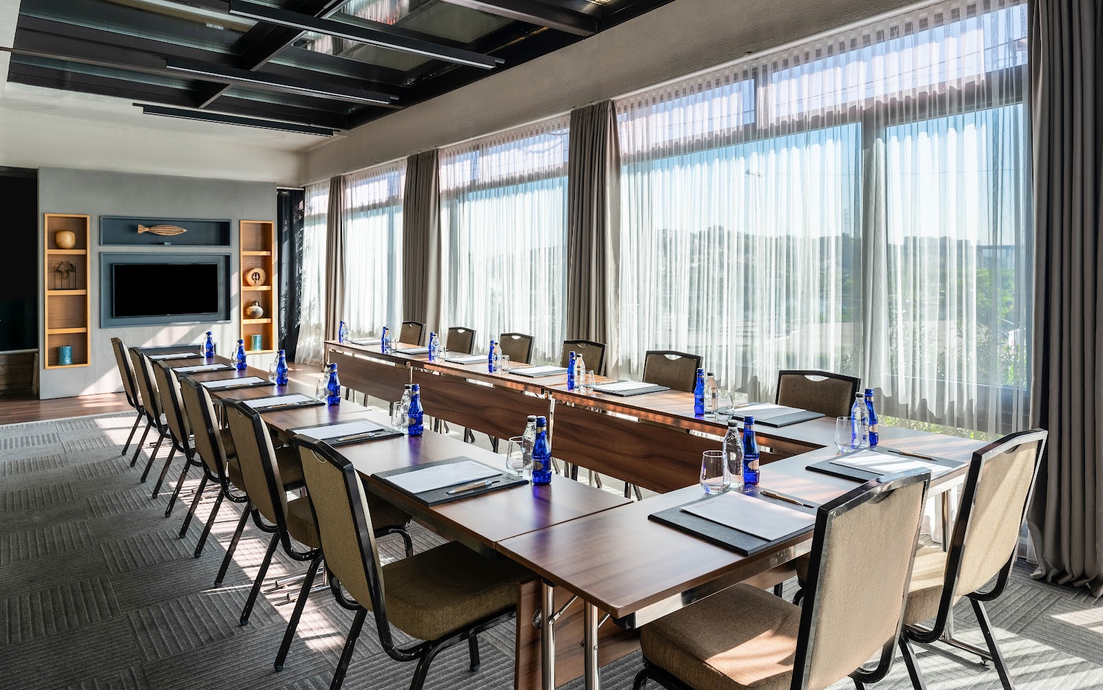 A professional meeting room set up in a U-shape configuration, with large windows overlooking the city.