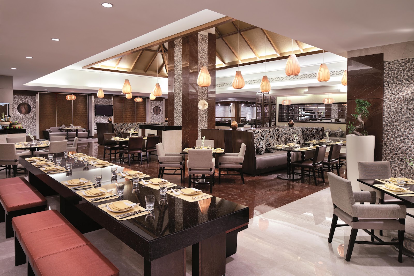 A modern and spacious restaurant interior with contemporary lighting fixtures, diverse seating arrangements including long communal tables and individual tables, showcasing a sophisticated and inviting atmosphere.