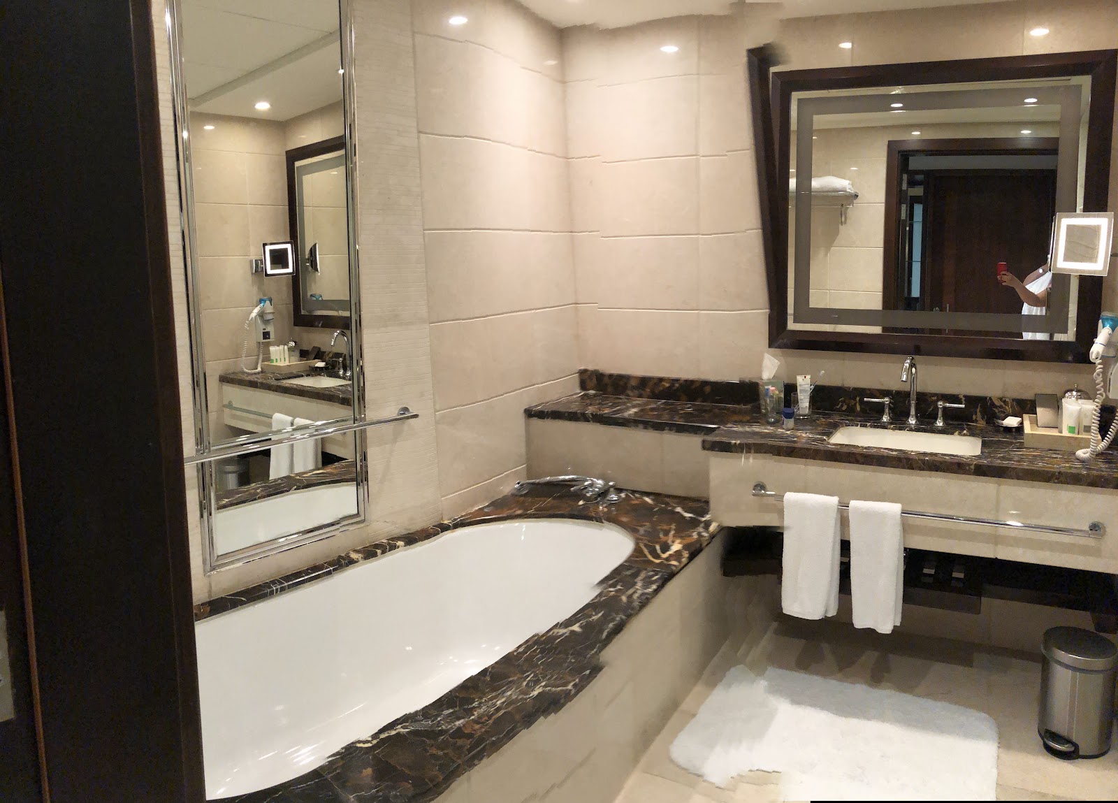 A spacious and luxurious private bathroom featuring a deep-set bathtub with elegant marble surround, a large vanity with a single basin, and an ornate framed mirror, reflecting the high-end finishes.