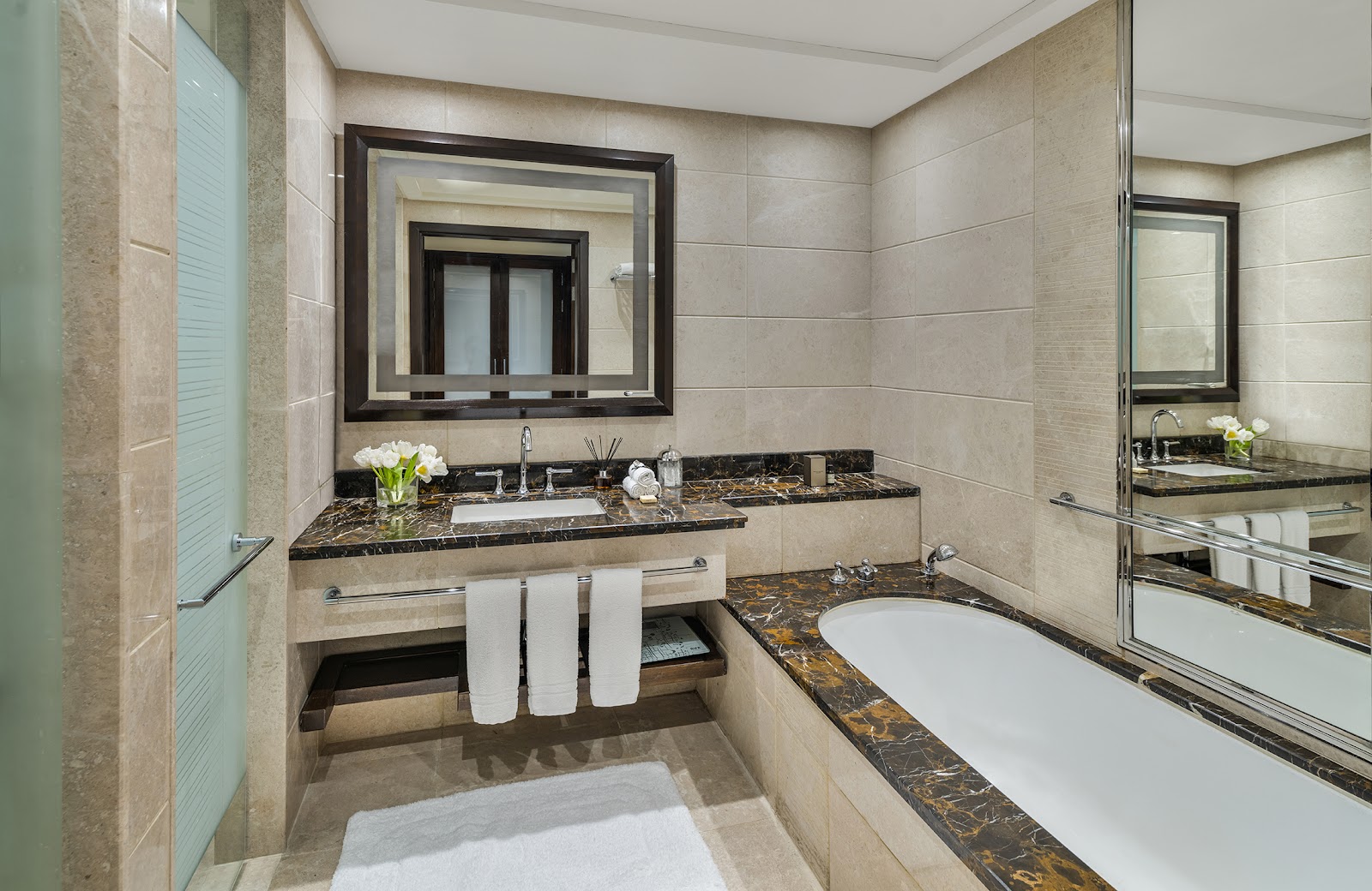 Another elegant private bathroom with a contemporary design, featuring a built-in bathtub with marble accents, a sleek vanity, and a separate walk-in shower area behind a frosted glass partition.