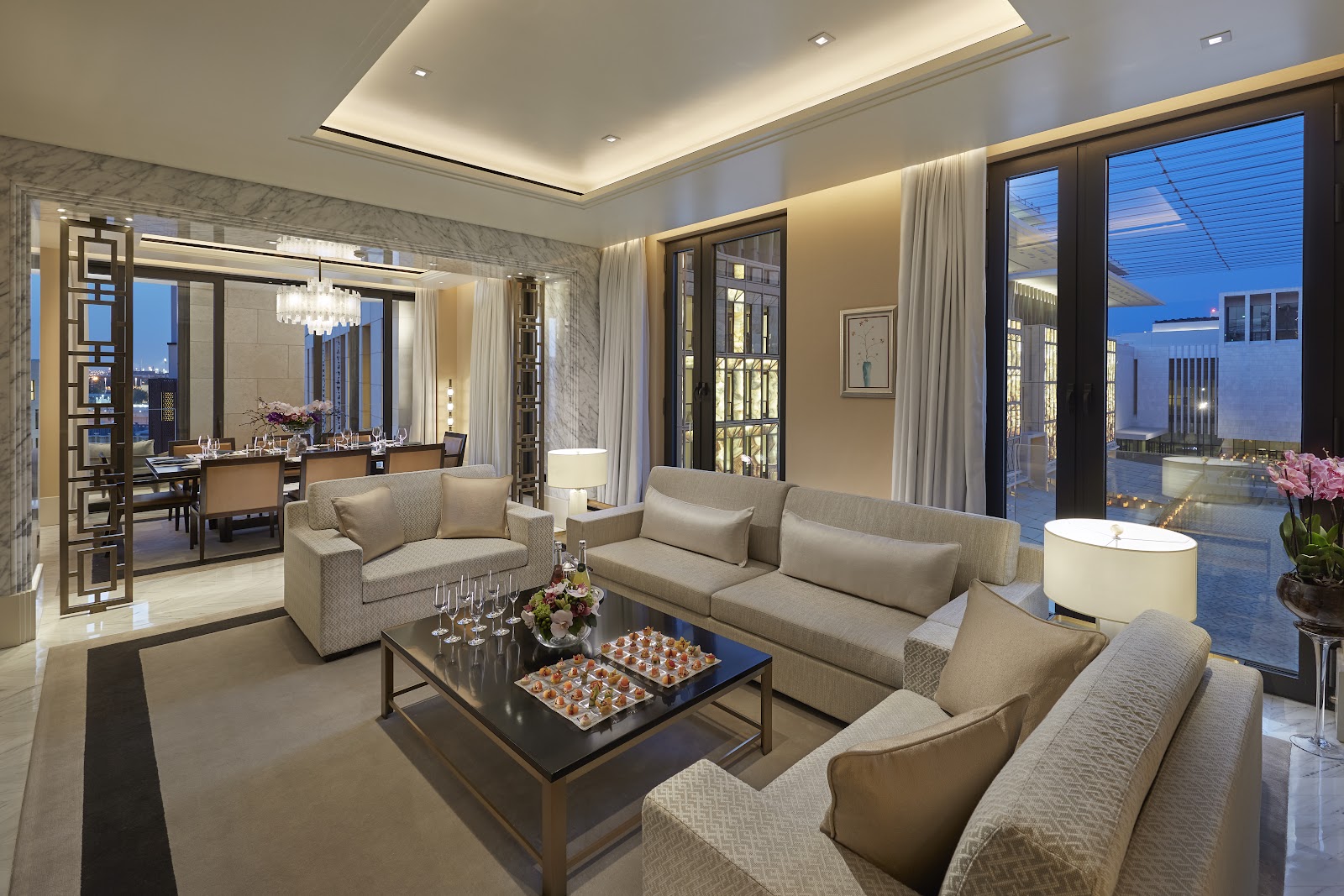 A spacious and luxurious living room of a suite, with a separate dining area and access to a private terrace.