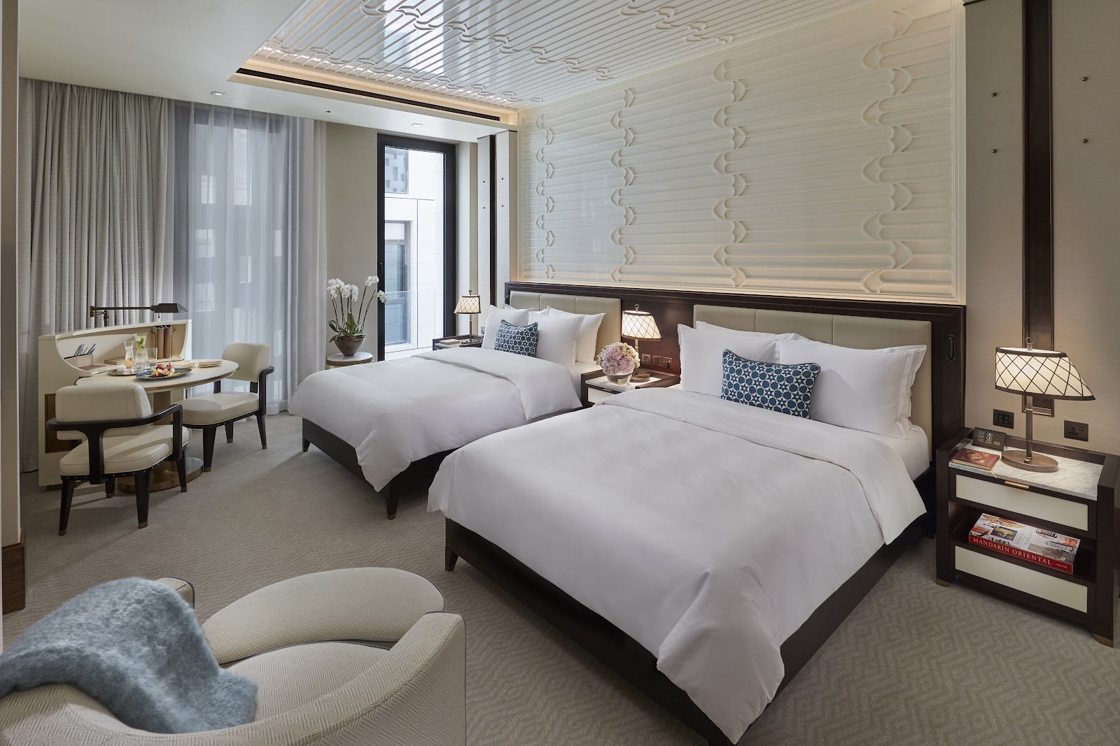 A luxurious hotel room with two twin beds, an elegant seating area, and modern decor.