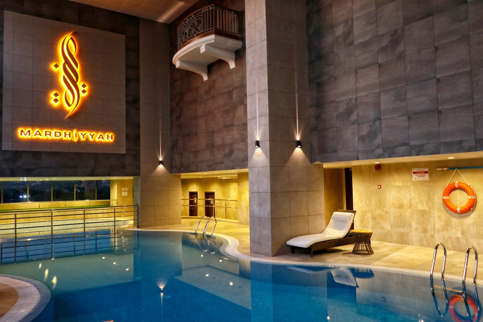 A large indoor swimming pool with high ceilings, prominent hotel branding, and a relaxing lounge chair, offering an enclosed swimming environment.