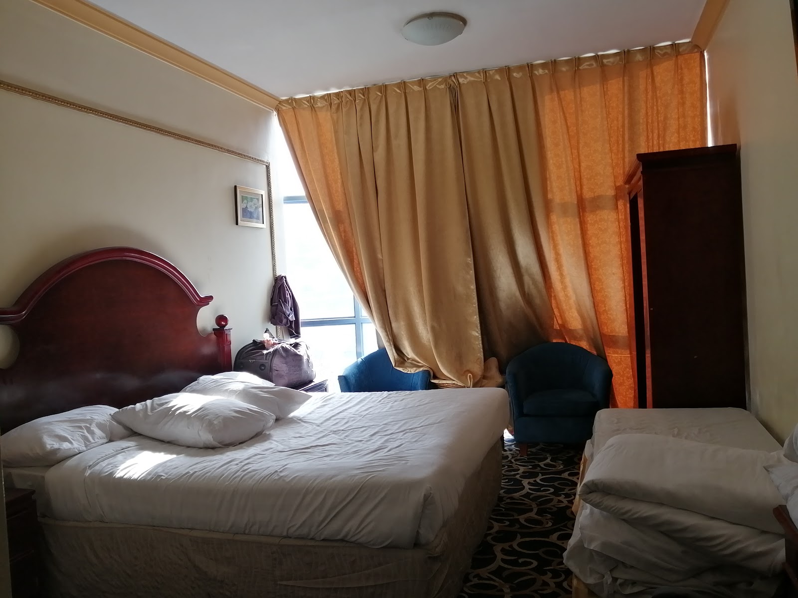 A standard hotel room with a queen-sized bed, additional bedding, a wardrobe, and seating, designed for pilgrim comfort.