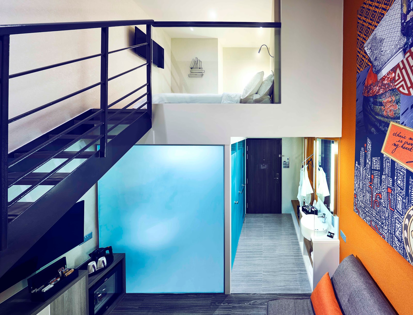 The lower level of a loft-style room, featuring an entrance, a vanity/desk area, and a staircase leading to an upper bedroom visible through glass.