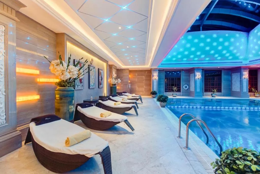 An elegant indoor swimming pool area with numerous lounge chairs and sophisticated blue and white lighting, currently empty.