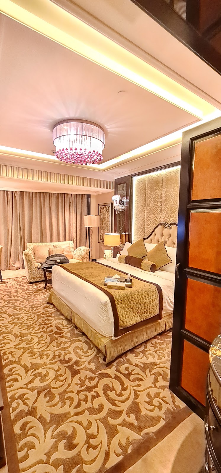 A luxurious hotel room featuring a king-sized bed with plush bedding, an elegant seating area with a sofa, and sophisticated traditional decor.