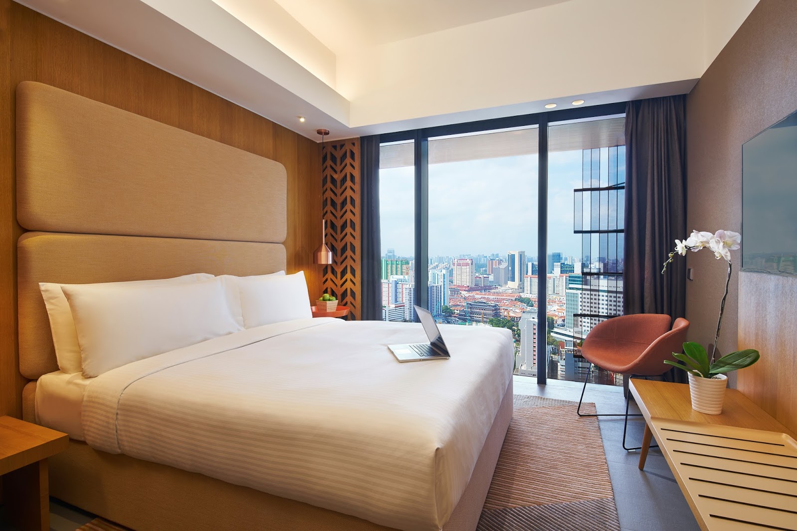 A bright hotel room with a king-sized bed, large window offering city views, and modern furnishings.