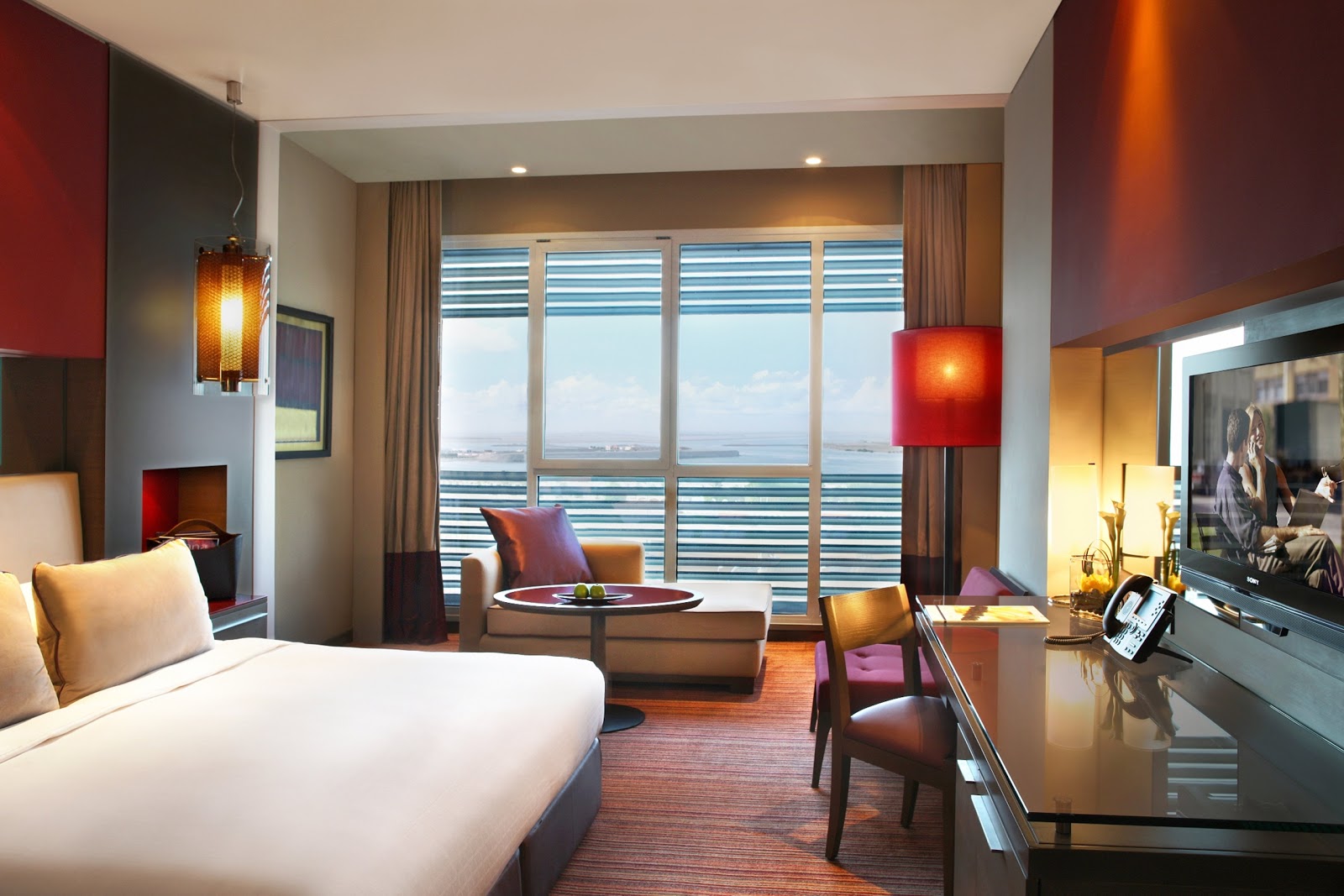 A stylish hotel room with a king-sized bed, separate seating area, and a large window offering a distant view.