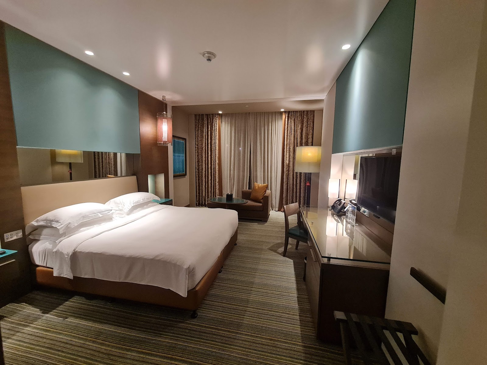 A comfortable hotel room with a king-sized bed, desk, and armchair, featuring contemporary decor.