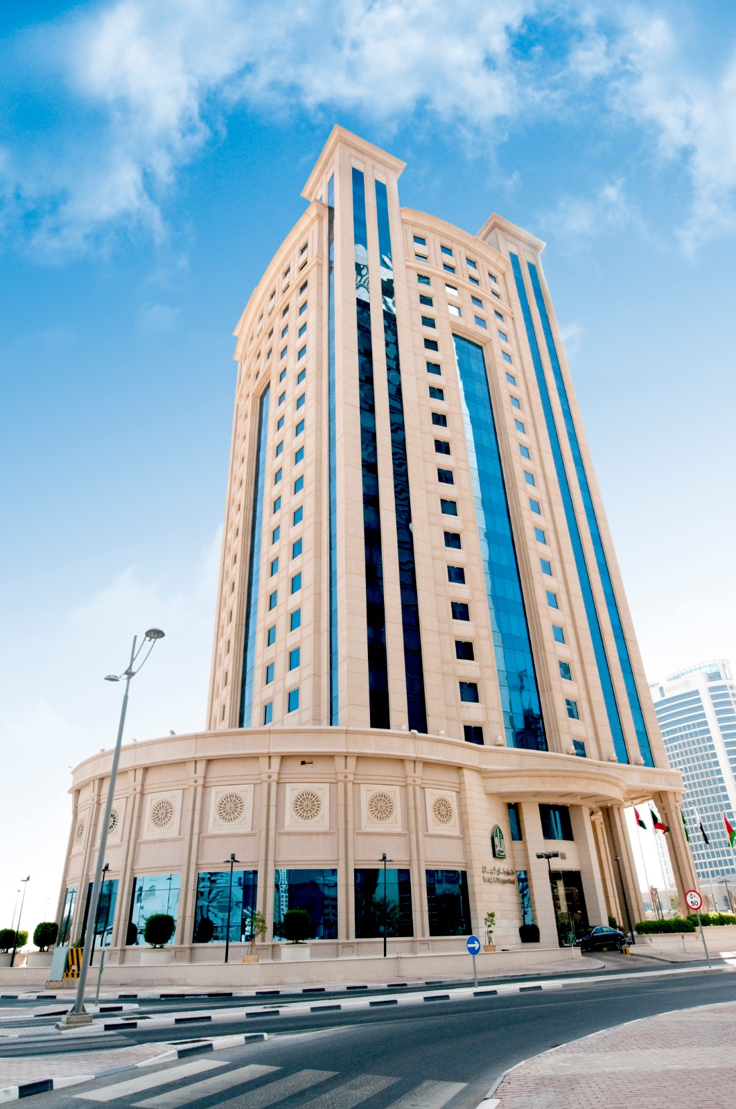 A sunny daytime street-level view of the tall, modern Retaj Al Rayyan Hotel building against a clear blue sky.