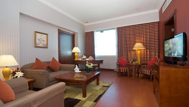 A spacious living room area within a hotel suite, featuring a sofa, armchairs, a coffee table, and a television.