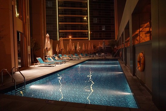 Illuminated outdoor swimming pool at Rove Dubai Marina, surrounded by loungers at night.