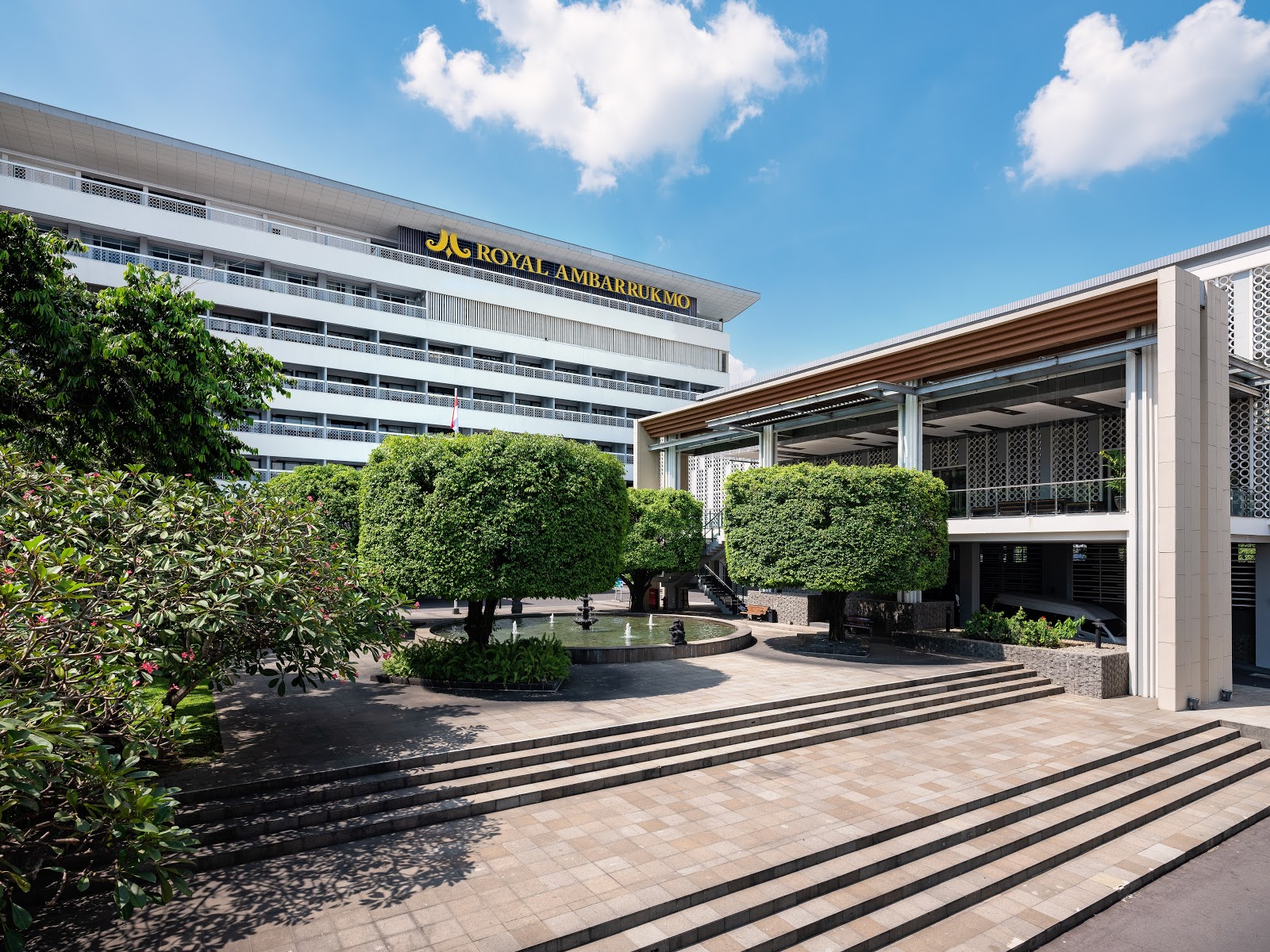 A daytime view of Royal Ambarrukmo Yogyakarta's modern building facade and spacious outdoor courtyard entrance area.