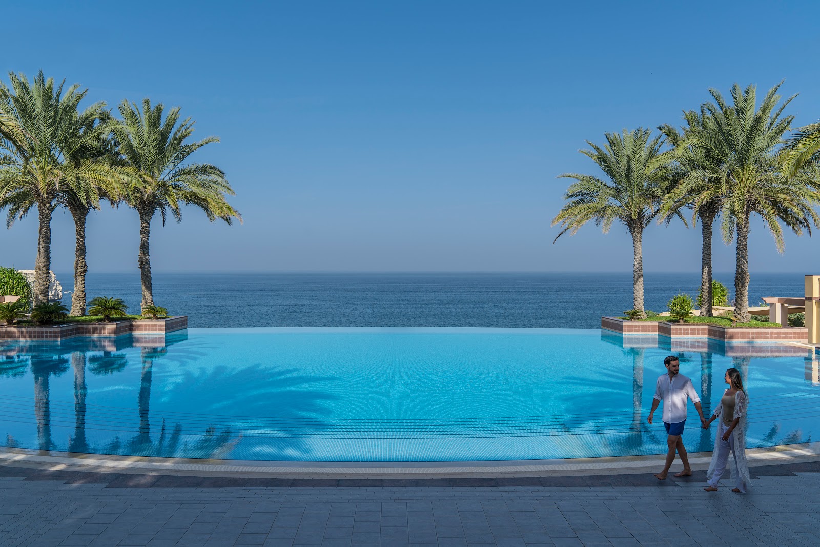 An expansive infinity pool offering breathtaking views of the Arabian Sea, framed by lush palm trees, with a couple walking at the edge.