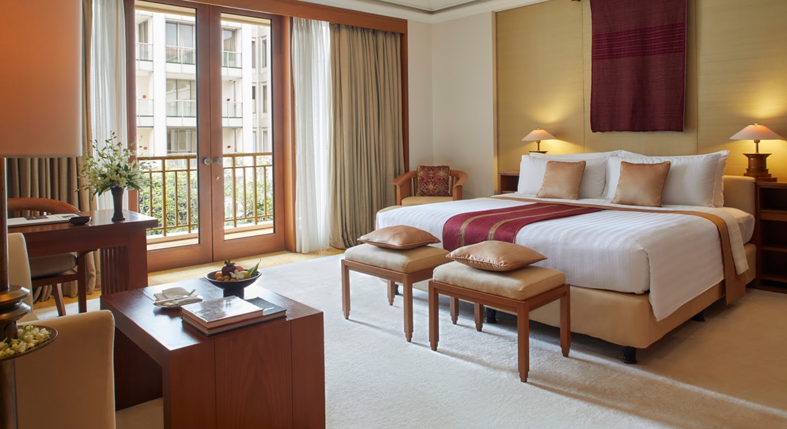 A luxurious and spacious hotel room with a king-size bed, a comfortable seating area, a desk, and a private balcony overlooking green surroundings.